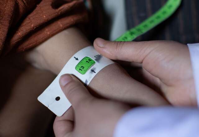 IRC mobile health team counsellor Ruqia Moqtased examines 2 year-old Samia with MUAC tape; the green color indicates she has recovered from acute malnutrition.