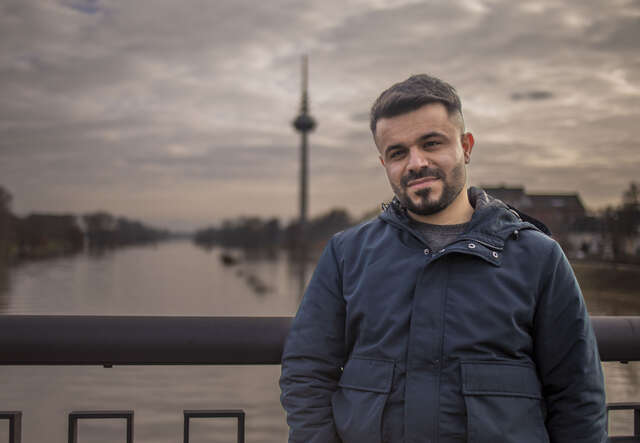 Ein junger Mann steht auf einer Brücke am Fluss.