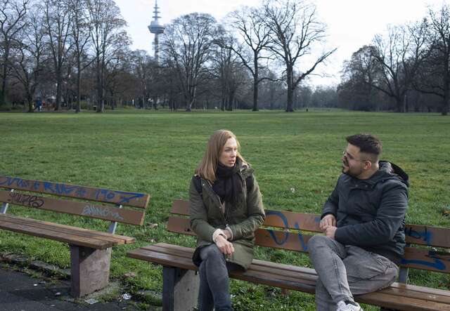 Zwei Personen sitzen auf einer Bank in einem Park.