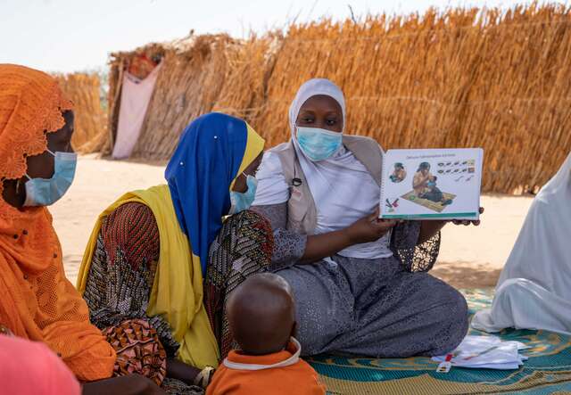 An IRC staff member teaches a course on proper child nutrition methods to new mothers who sit nearby and listen attentively.