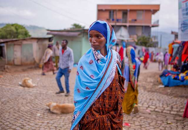 A woman with a blue headscarf walks through a market in Deder, Ethiopia.