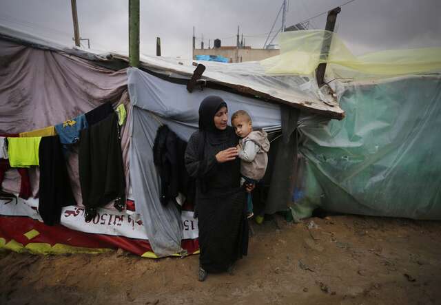 A woman holds a young child outside a makeshift shelter in Gaza.