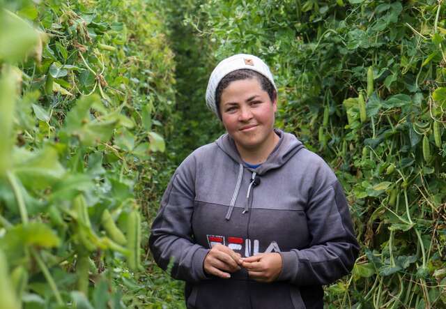 A woman poses for a photo in a field in Ecuador. She smiles softly.