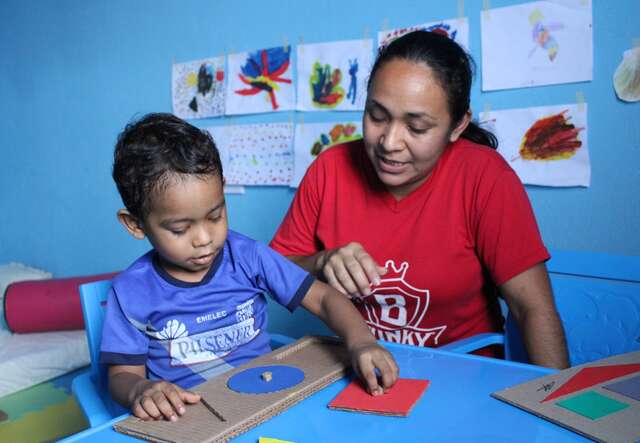 A mother sits next to a child and helps him with a learning activity.
