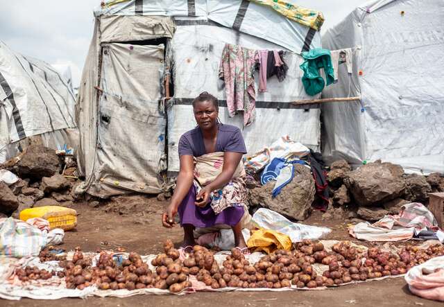 A woman sits in front of an array of potatoes outside of her shelter in a camp for displaced peoples in the DRC.