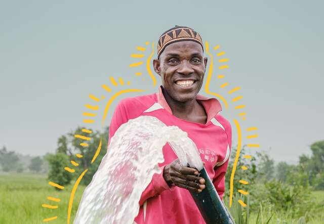 A smiling man pours water from a hose at his farm in Nigeria.