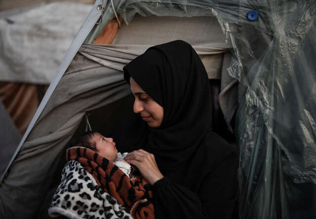 Kvinna i Gaza med sin nyfödda bebis i famnen utanför ett tält.