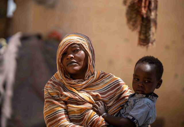 Altuma, 45, and her child stand in their roofless shelter, having fled war in Khartoum.