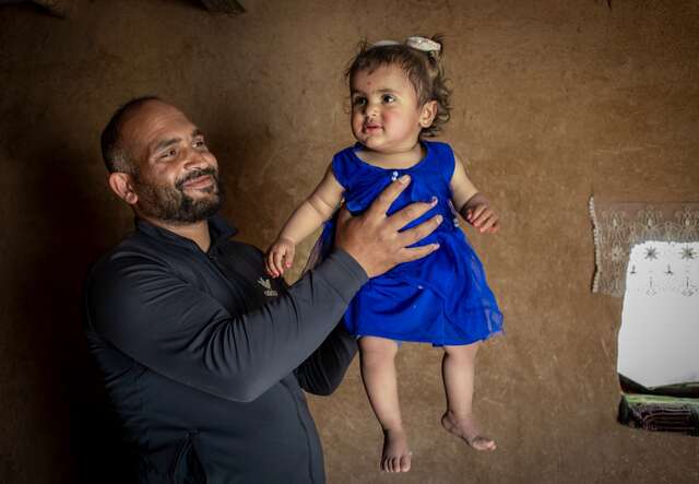 En pappa lyfter sin yngsta dotter i luften i deras hem i Syrien, båda ler.