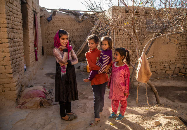 Fyra flickor står tillsammans framför ett enkelt hus i Afghanistan, där det pågår en humanitär kris. 