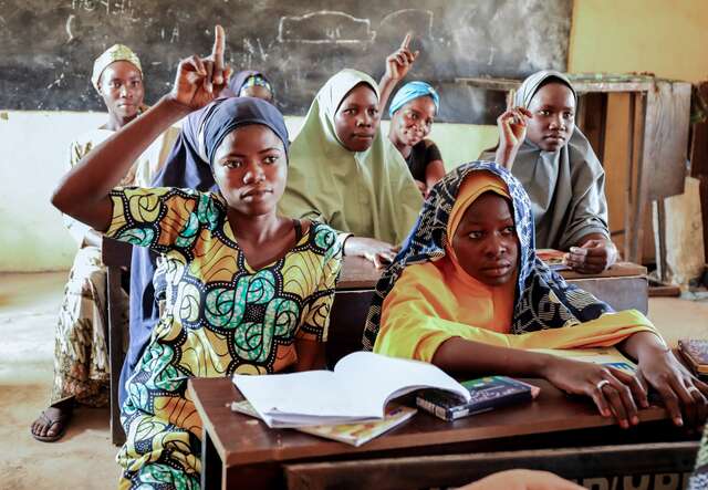 Several girls raise their hands to answer a question in their classroom in Nigeria.