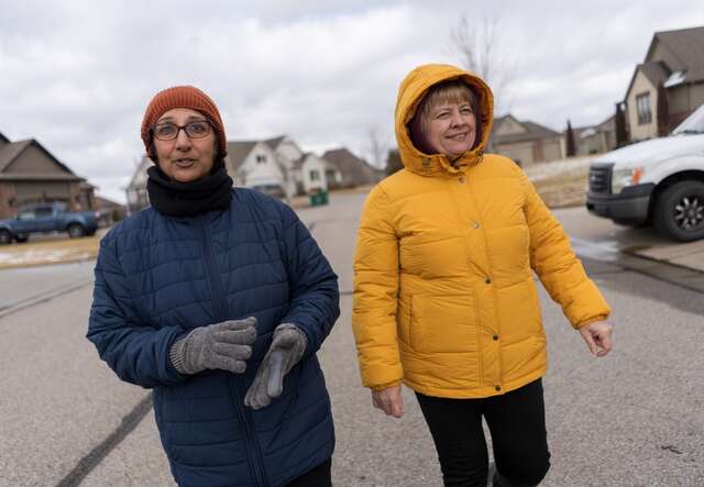 Two women walk down the street together in Wichita, Kansas. They share a smile and are dressed in warm clothes.