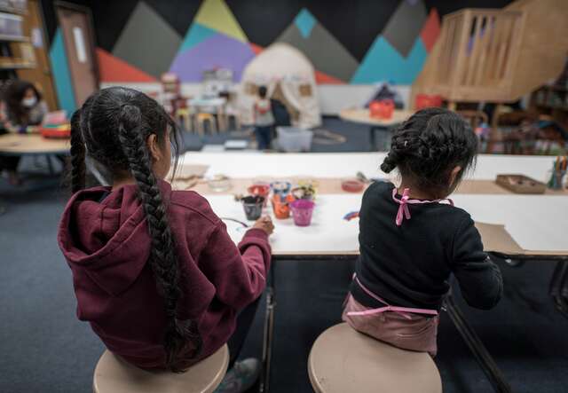 Two children sit and work on an arts and crafts project. Their back is to the camera to protect their identity.