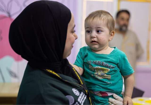 Duha holds a child in her arms after performing a medical checkup at the IRC clinic.