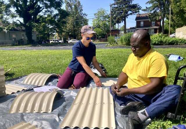 Two people sitting outdoors making items from bamboo.