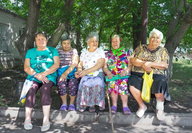Five older women sitting on a bench and smiling at the camera
