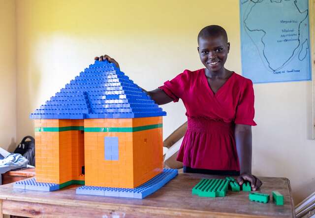 Girl stands next to a house made from Lego bricks