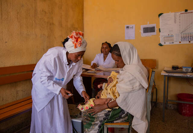 En av RESCUS sjukvårade ger ett litet barn vaccin som sitter i sin mammas knä.