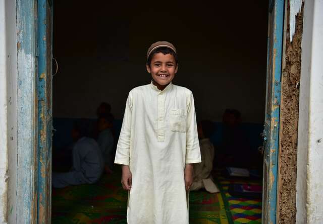 Attiq, 12, an Afghan refugee, stands at the entrance of an EU-supported IRC Accelerated Learning Program centre