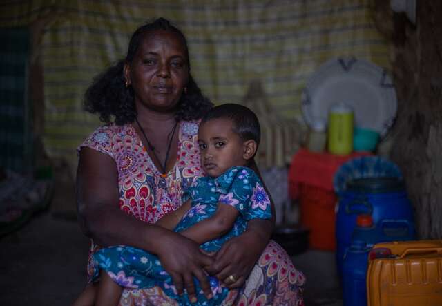 A mother holds her daughter in her lap. They sit inside their home in Ethiopia.