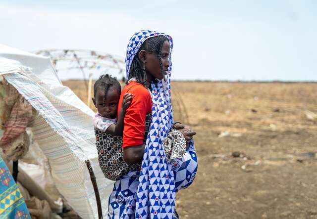 A mother is carrying her child while leaving their temporary shelter in Sudan.