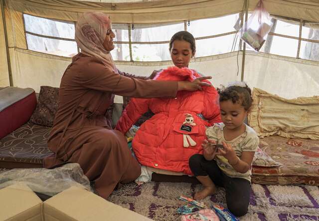 A mother and her two children try on new winter clothes they received from the IRC.