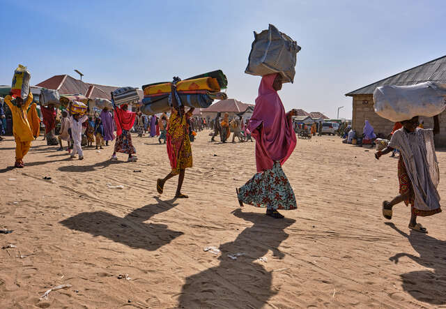 Människor går med sina ägodelar genom ett flyktingläger.