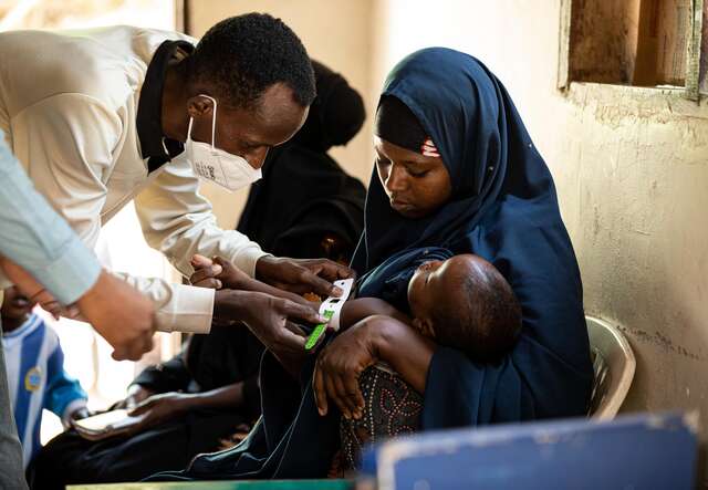 Health care workers taking MUAC measurements of Shukri’s son 