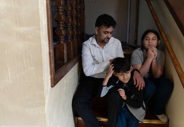 A family sit together on the steps of their home and pose for a photo.