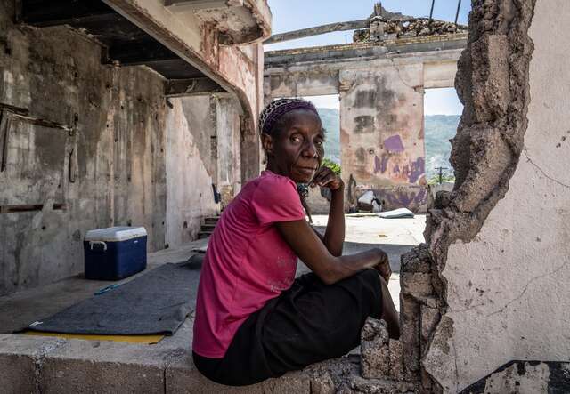 A woman poses for a picture in the remnants of a destroyed building in Haiti.