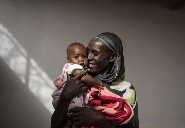 한 수단 여성이 아기를 안고 환하게 웃고 있습니다.