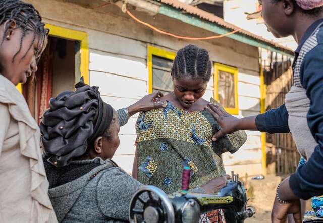 Foster siblings help Fatuma take measurements for a new dress she is sewing for Gentille.
