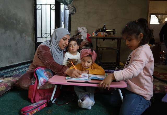 Bayan sits with her daughters after school, guiding them through their studies in their home, her sewing machine pictured in the back.