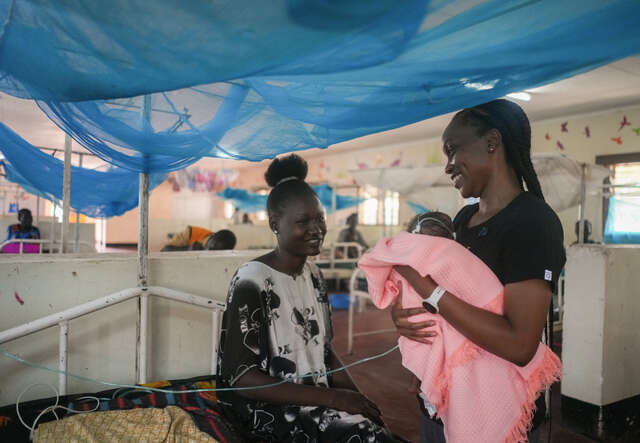 IRC Health Manager Dr. Sila holds newborn baby Blessing and talks with her mother Hiba.