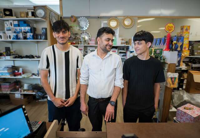 Three men pose for a photo behind a shop counter.