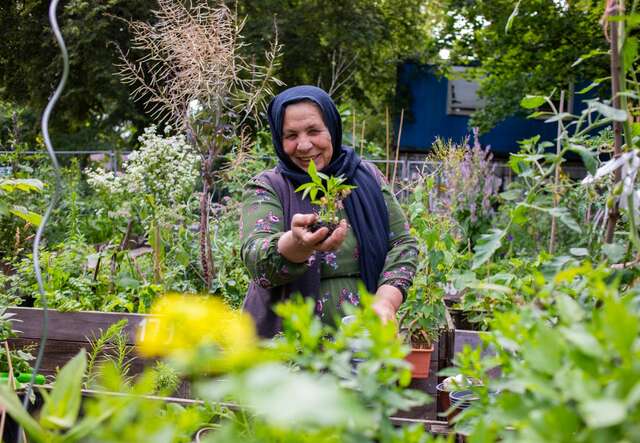 Faisha sitter i en trädgård och håller upp en planta. 