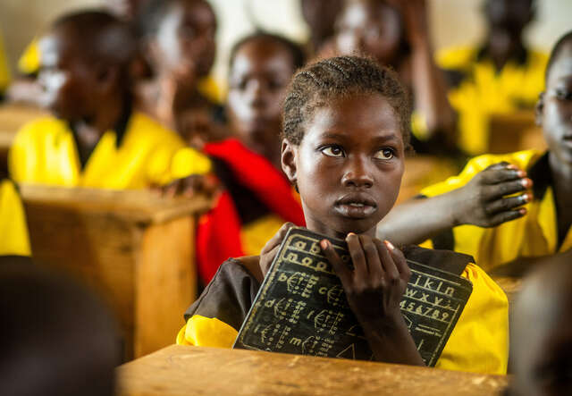 En flicka sitter i ett klassrum och skriver i en bok.
