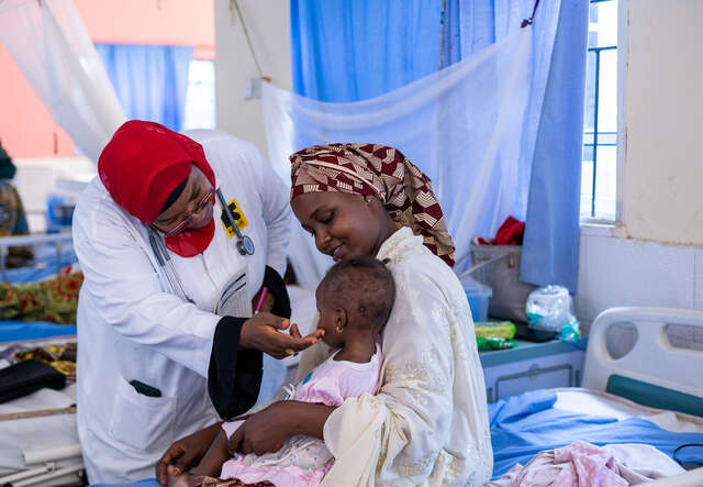 En RESCUE vårdpersonal ger en liten flicka medicin medan flickan sitter i famnen på mamman på en vårdavdelning.