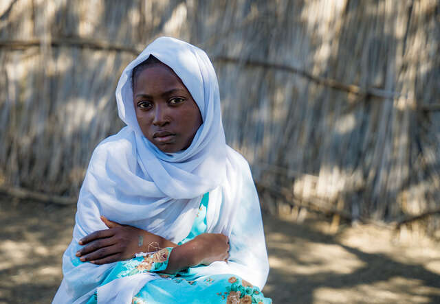 En ung flicka sitter på marken med händerna i kors. 
