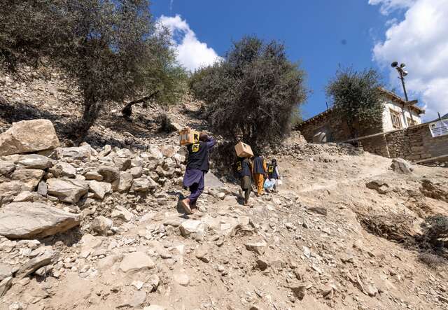 IRC health workers carry medical supplies on their shoulders to a rural Afghan village.