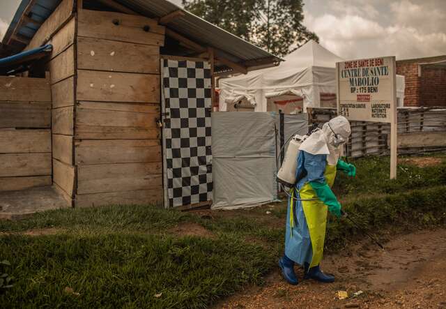 A health worker in full protective gear sprays disinfectant outside a health center in Beni, DRC.