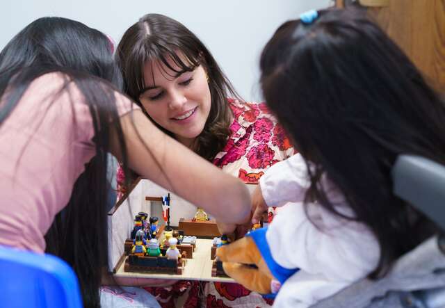 An IRC legal assistant shows two young girls how a US immigration court works by demonstrating with a LEGO model of a courtroom.