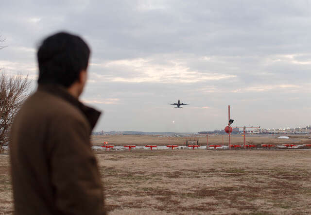 A man looks on as a plane takes off at an airport.