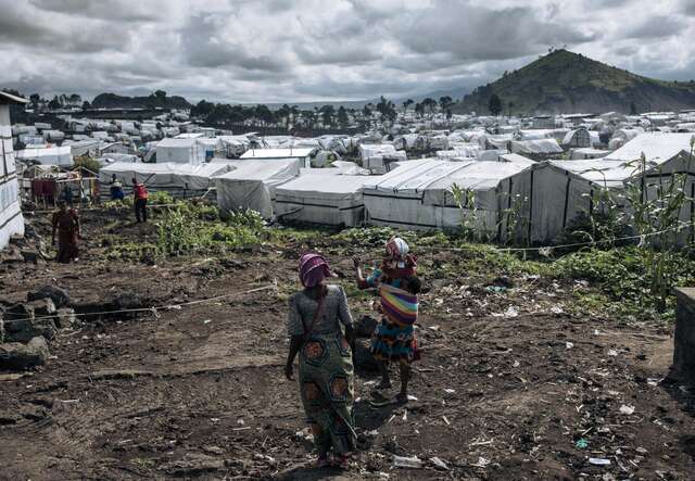Two people walk through a refugee camp in the DRC.