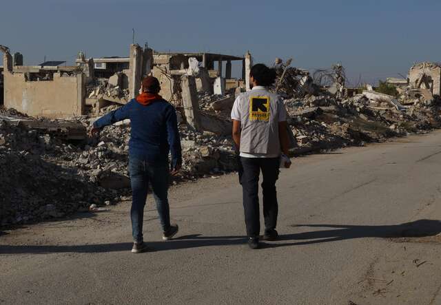 An IRC staff member and a client walk through a devastated neighborhood in Syria.