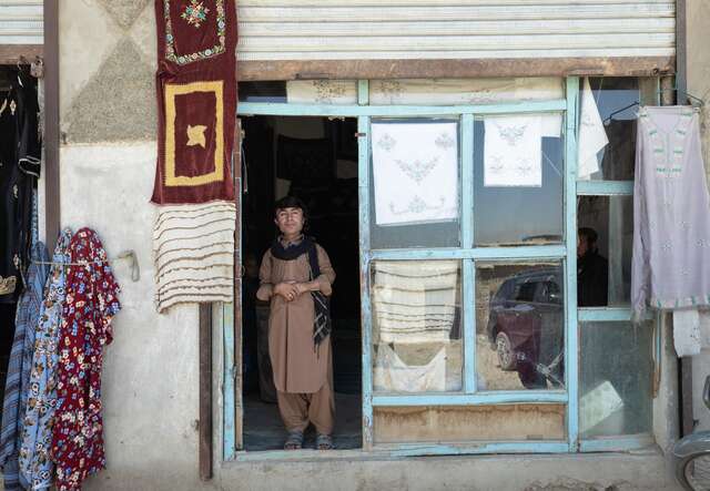 Darweza stands at the entrance of the tailor shop where he works. 