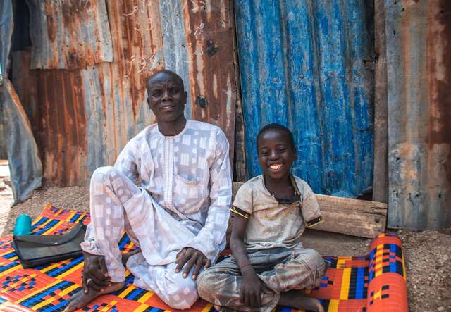 Yahaya and  Ibrahim sitting in front of their home, smiling at the camera.