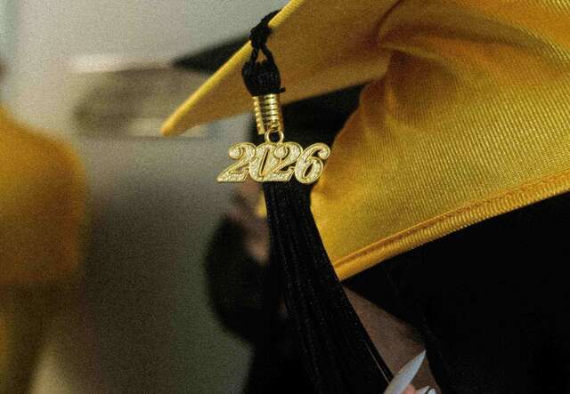 A Kickstart graduate holds the tassel of their graduation cap with a gold "2026" charm.