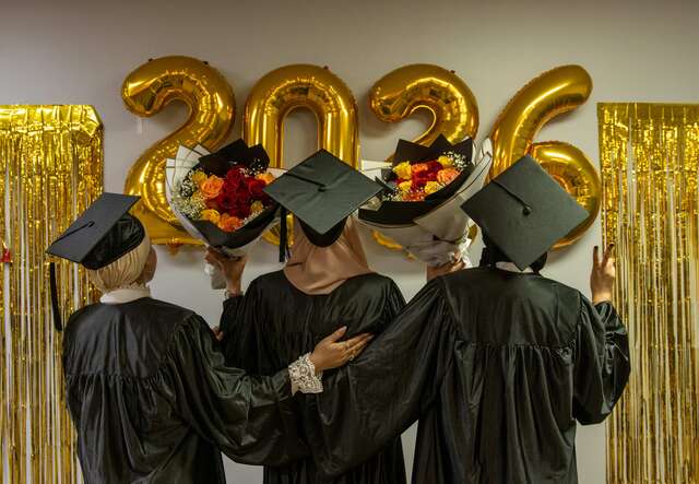 Three Kickstart grads look at golden graduation balloons with the numbers "2026".