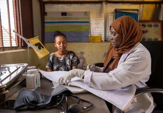 IRC midwife Zakia Yaqoup reviews patient records at a desk while Samher, 19, sits across from her at a clinic in Gedaref, Sudan.